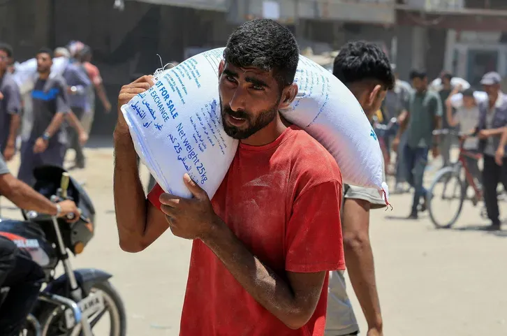Ein Palästinenser trägt einen Sack Mehl, während sich Menschen in Khan Younis im südlichen Gazastreifen versammeln, um Hilfsgüter zu erhalten, 26. Juni 2025. REUTERS/Hatem Khaled Credit: Hatem Khaled/רויטרס