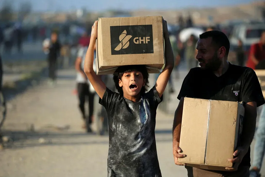 Menschen mit Hilfspaketen gehen am 25. Juni 2025 auf der Salah-al-Din-Straße in der Nähe des Flüchtlingslagers Nusseirat im nördlichen Gazastreifen entlang, die von Palästinensern auf der Suche nach Lebensmitteln genutzt wird, um eine von der privat geführten Gaza Humanitarian Foundation (GHF) eingerichtete Hilfsgüterausgabestelle zu erreichen. (Photo by Eyad BABA / AFP) Credit: AFP/EYAD BABA