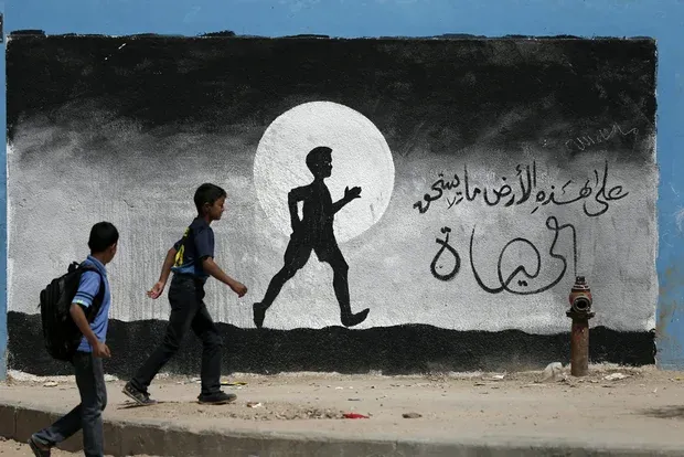 Palästinensische Jungen laufen an einem Graffiti an einer Wand der UN-Schule in Beit Hanoun im Gazastreifen vorbei (AFP)